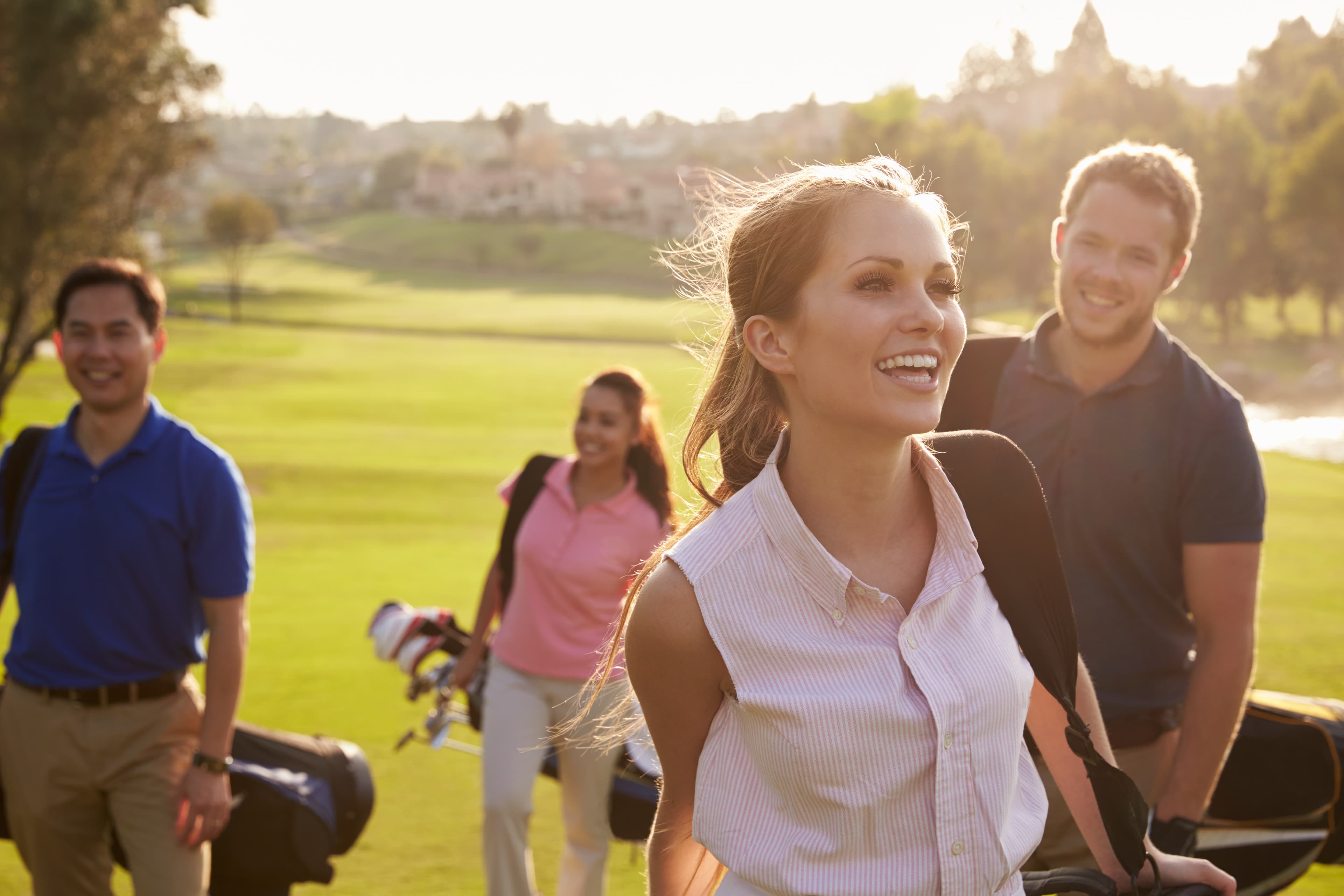 Golferin und Golfer tragen ihre Bags lachend über den Platz